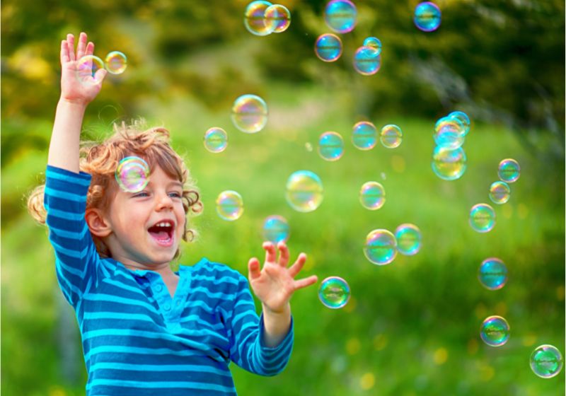 Das Bild zeigt ein lachendes Kind das mit Seifenblasen spielt.