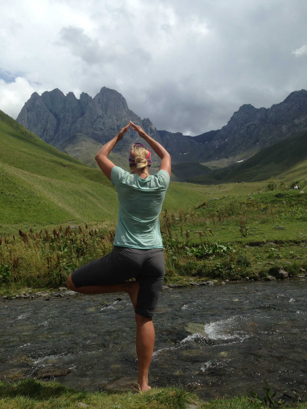 Das Bild zeigt Stephanie Schaffer am Fluss stehend in der Yoga-Position Baum.